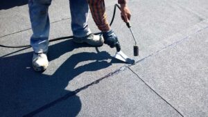A homeowner using a level on a shingle roof to check the slope angle on a sunny day.