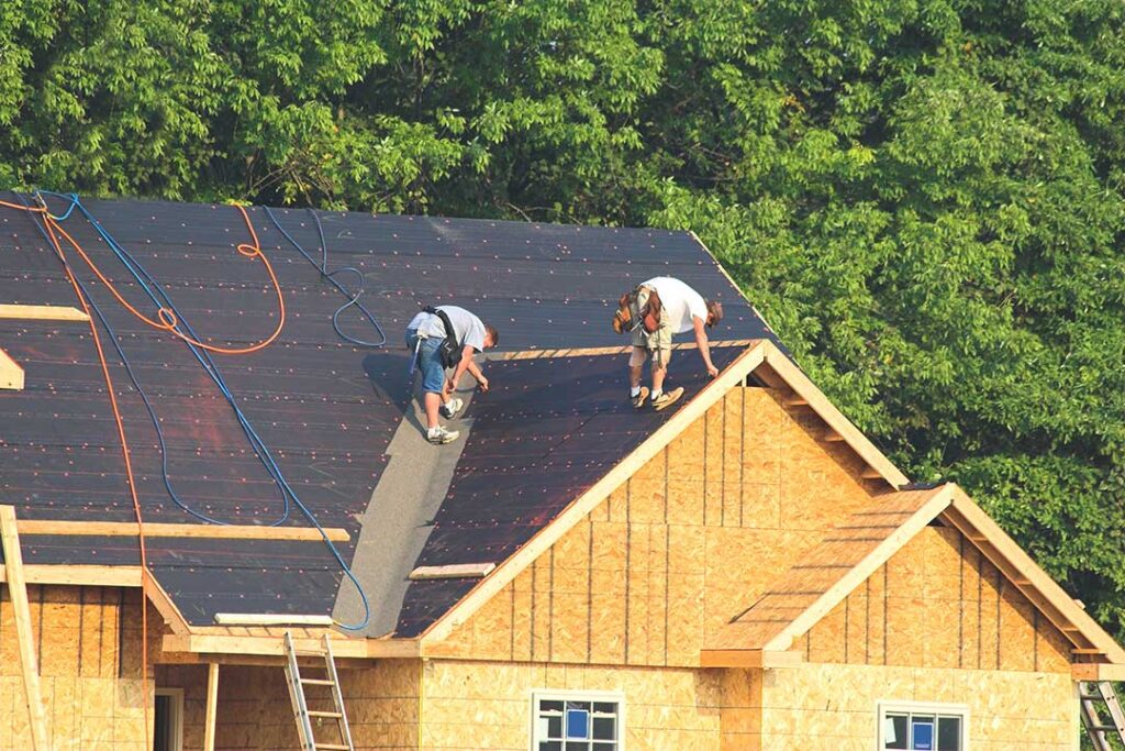 Homeowner examining an asphalt shingle roof with visible moss and minor damage in a suburban residential yard.