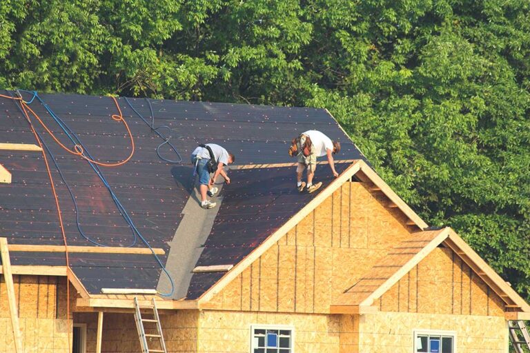 Homeowner examining an asphalt shingle roof with visible moss and minor damage in a suburban residential yard.